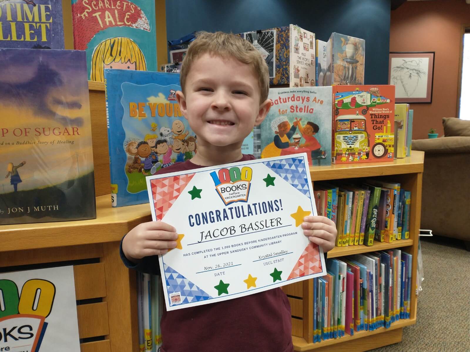 Young boy holding a sign that says he completed the 1,000 books before Kindergarten program.