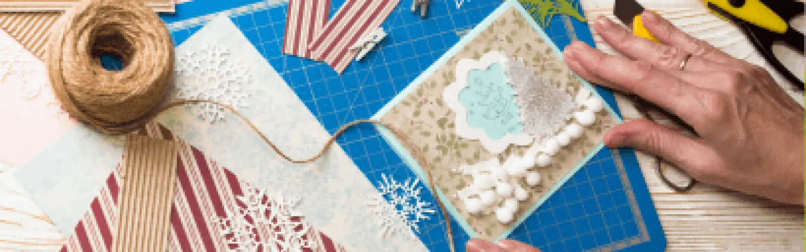 A pair of hands designing a card with other craft materials around. 