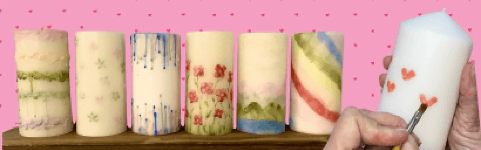 A row of candles with designs on them. A hand is painting a candle.
