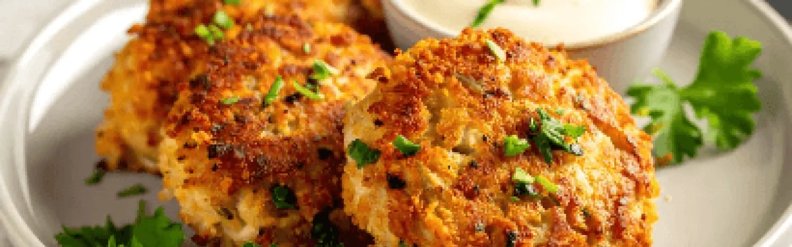 A plate with crab cakes and a small container of sauce. 